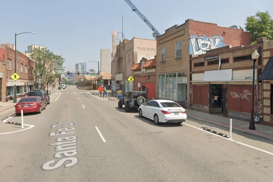 A view up Santa Fe Drive in Denver. Stores and construction are visible along the street, and Downtown Denver looms in the background.